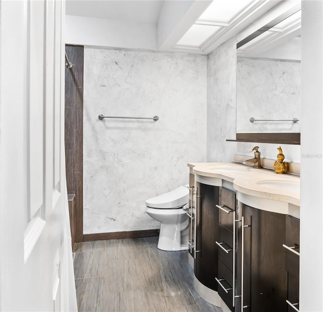 bathroom with toilet, vanity, wood finished floors, and baseboards