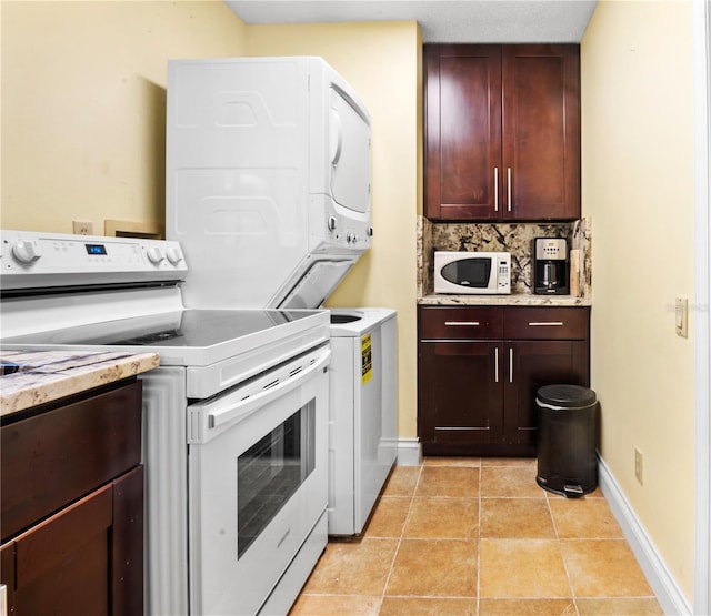 clothes washing area with baseboards, stacked washer and clothes dryer, laundry area, and light tile patterned floors