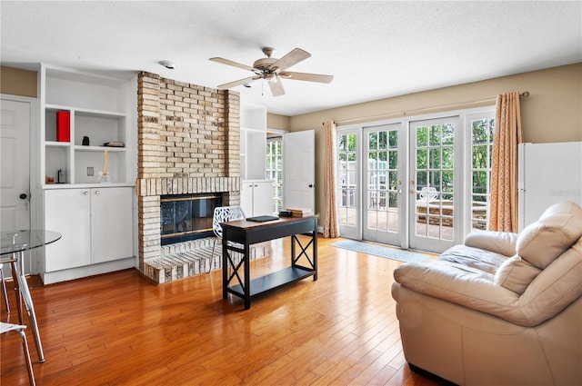 living room featuring light wood finished floors, a ceiling fan, a brick fireplace, and a textured ceiling
