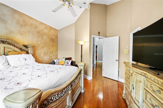 bedroom with high vaulted ceiling, wood-type flooring, baseboards, and a ceiling fan