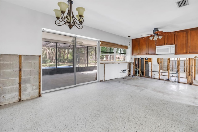 kitchen with brown cabinets, speckled floor, visible vents, white microwave, and ceiling fan with notable chandelier