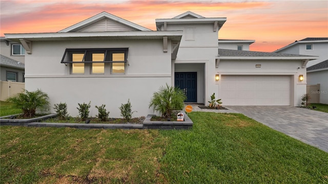 view of front of property featuring a garage, stucco siding, decorative driveway, and a lawn