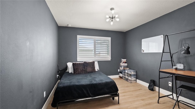 bedroom with light wood-style flooring, a notable chandelier, and baseboards