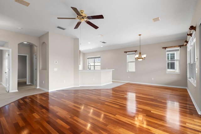 unfurnished living room with arched walkways, wood finished floors, ceiling fan with notable chandelier, baseboards, and visible vents