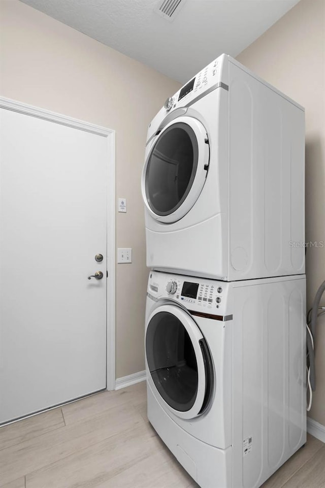 clothes washing area with light wood-style flooring, visible vents, stacked washer / drying machine, baseboards, and laundry area