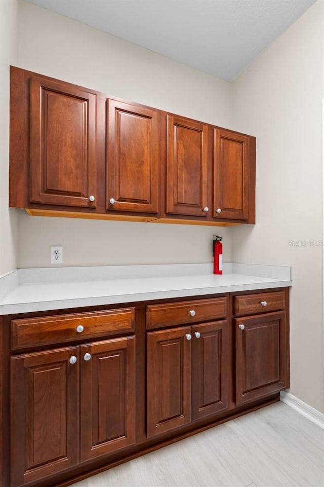 kitchen with baseboards, light wood-style flooring, light countertops, and brown cabinets