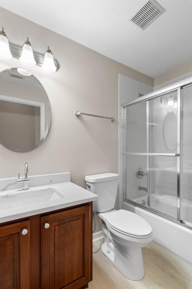 full bath featuring a textured ceiling, visible vents, enclosed tub / shower combo, toilet, and vanity