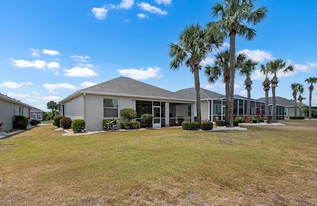 back of property with stucco siding, a sunroom, and a lawn