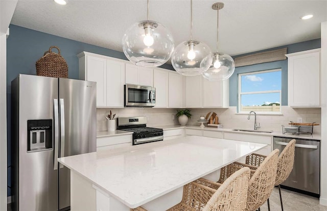 kitchen featuring white cabinets, a center island, a sink, backsplash, and appliances with stainless steel finishes