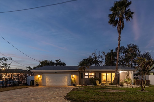 single story home featuring a lawn, an attached garage, fence, and decorative driveway