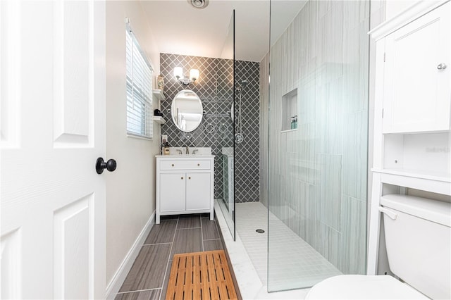 full bath featuring a tile shower, toilet, vanity, and baseboards
