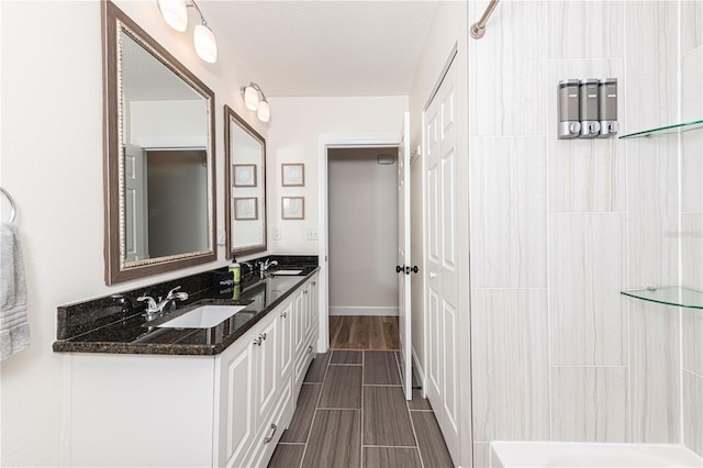 bathroom with double vanity, wood finish floors, a shower, and a sink