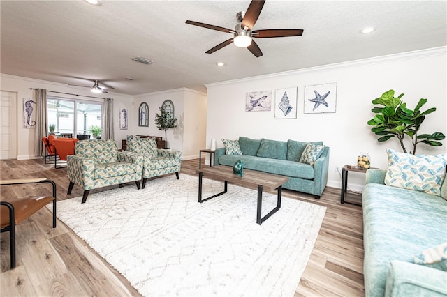 living room featuring light wood finished floors, a textured ceiling, visible vents, ceiling fan, and crown molding