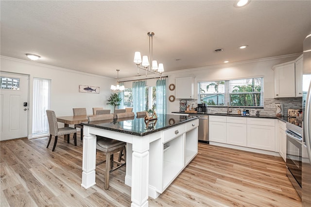 kitchen with light wood finished floors, dishwasher, ornamental molding, decorative backsplash, and a chandelier