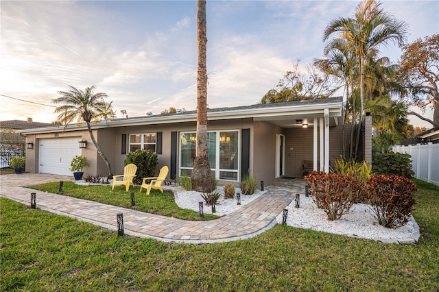 ranch-style home featuring fence, a garage, a front yard, and stucco siding