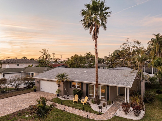 ranch-style home featuring an attached garage, fence, decorative driveway, and roof with shingles