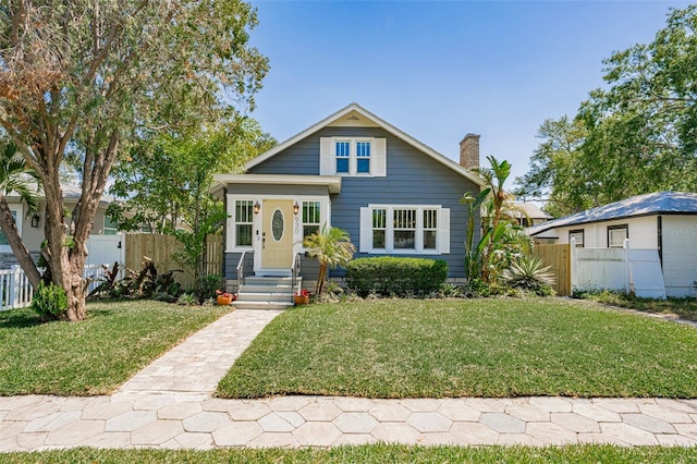 bungalow-style house with fence, a chimney, and a front yard