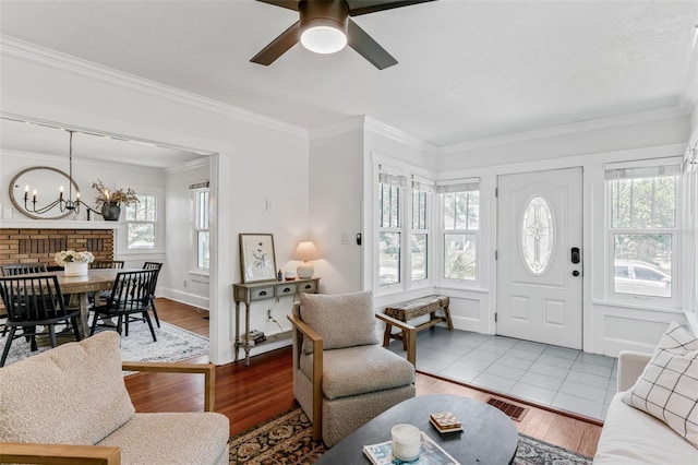 living room with ceiling fan with notable chandelier, wood finished floors, ornamental molding, and visible vents