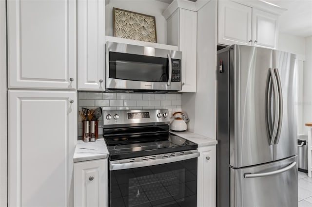 kitchen featuring light stone counters, stainless steel appliances, light tile patterned flooring, decorative backsplash, and white cabinetry