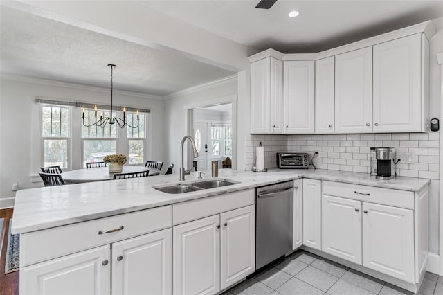 kitchen featuring a peninsula, stainless steel dishwasher, a sink, a chandelier, and ornamental molding
