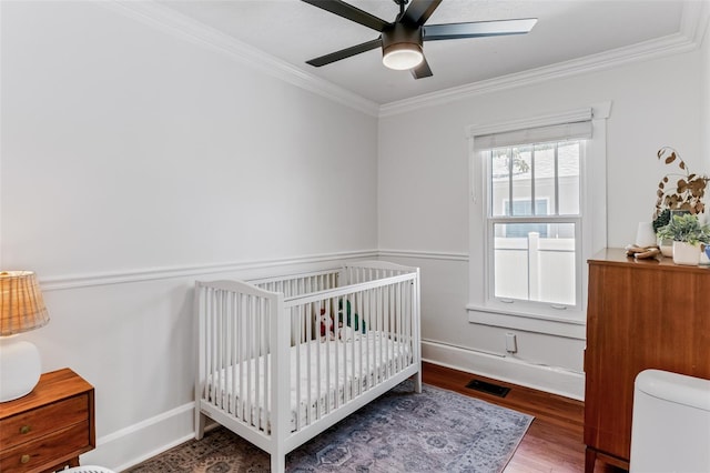 bedroom with wood finished floors, a nursery area, crown molding, baseboards, and ceiling fan