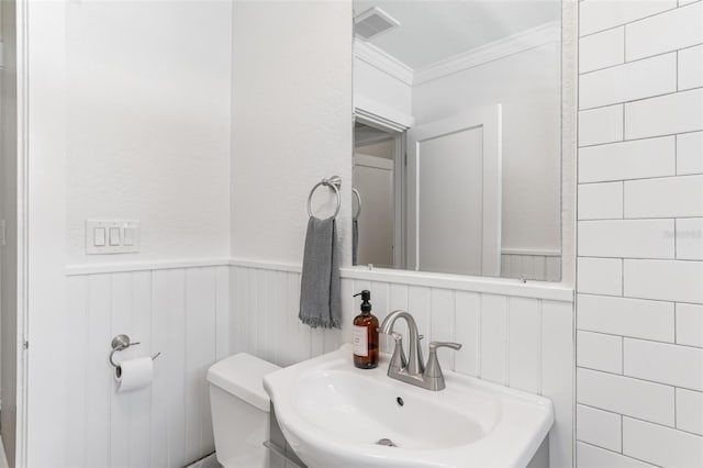 bathroom featuring a wainscoted wall, a sink, toilet, visible vents, and ornamental molding