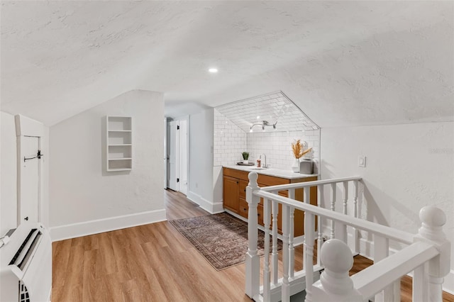 bonus room with a sink, a textured ceiling, light wood-style floors, baseboards, and lofted ceiling