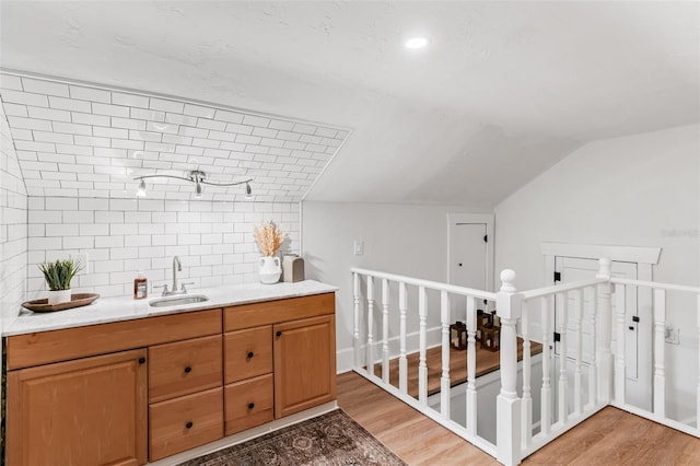 interior space featuring a sink, light wood-type flooring, vaulted ceiling, decorative backsplash, and light countertops