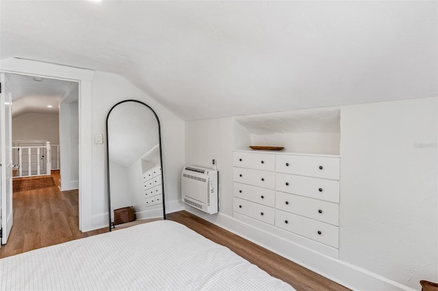 bedroom with vaulted ceiling, wood finished floors, heating unit, and baseboards