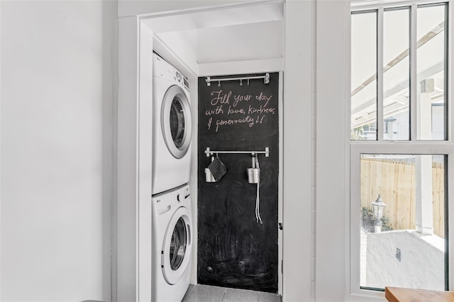 clothes washing area with a wealth of natural light, stacked washer / dryer, tile patterned floors, and laundry area