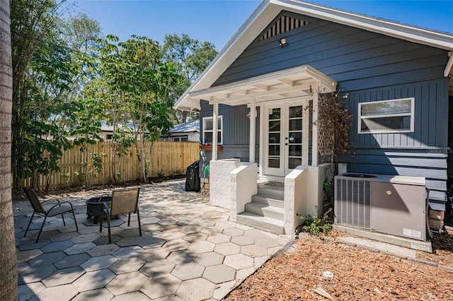 rear view of house with central AC, a patio area, board and batten siding, french doors, and fence