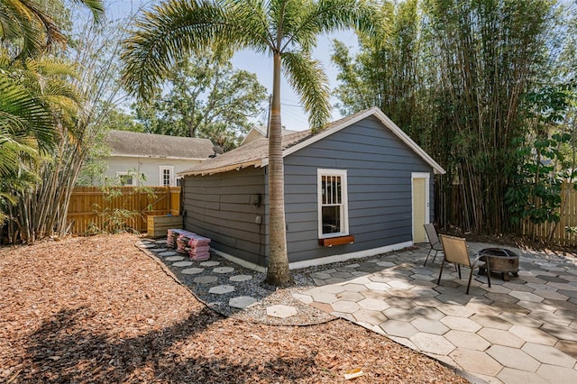 back of house featuring fence, a shingled roof, an outdoor structure, a patio, and an outdoor fire pit