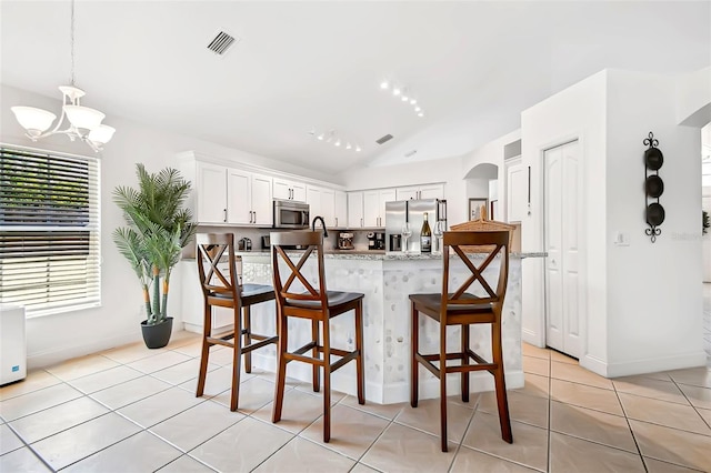kitchen with stainless steel appliances, arched walkways, vaulted ceiling, a kitchen breakfast bar, and white cabinets