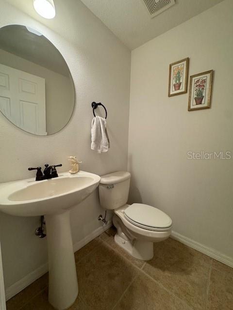 half bath with baseboards, toilet, and visible vents