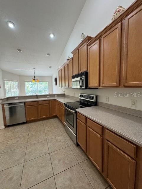 kitchen featuring brown cabinets, light tile patterned floors, light countertops, a sink, and stainless steel appliances