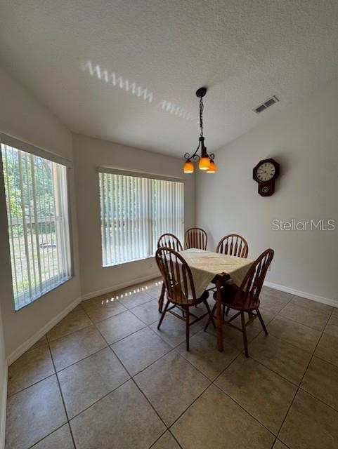 dining room featuring an inviting chandelier, tile patterned flooring, visible vents, baseboards, and a textured ceiling