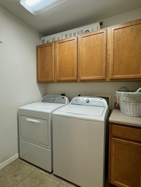 laundry room with cabinet space, independent washer and dryer, baseboards, and light tile patterned floors
