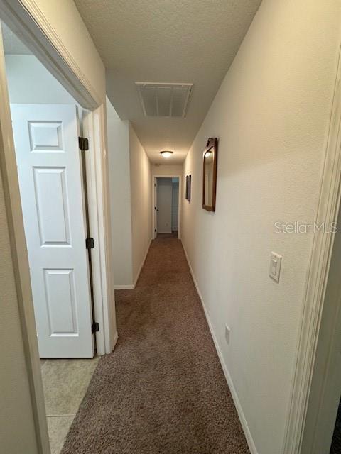corridor with attic access, a textured ceiling, visible vents, baseboards, and light carpet