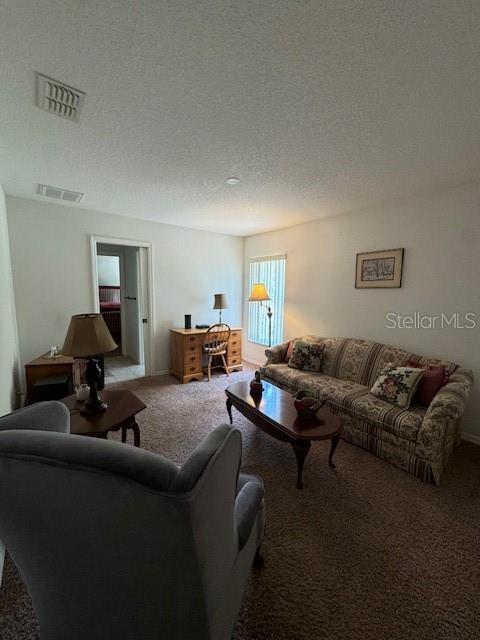 carpeted living area with visible vents and a textured ceiling