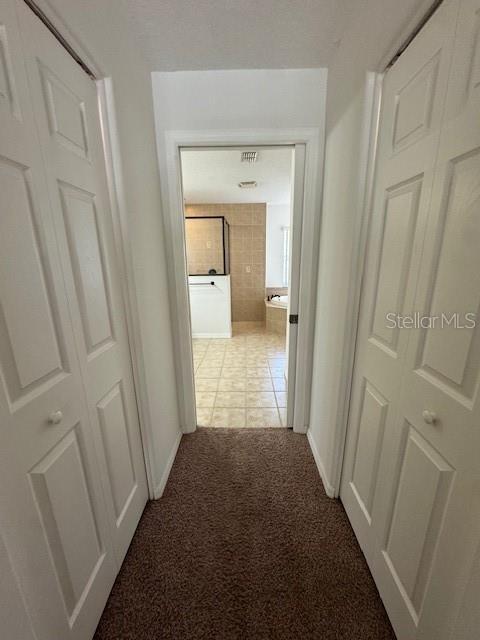 corridor with light tile patterned floors, baseboards, and light colored carpet