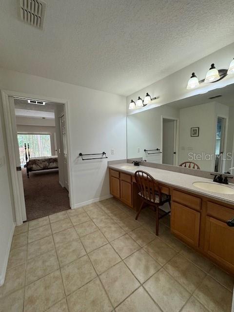 ensuite bathroom featuring a textured ceiling, visible vents, tile patterned flooring, vanity, and baseboards