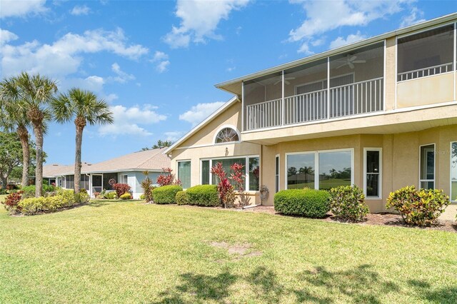 rear view of property featuring a lawn, ceiling fan, and stucco siding