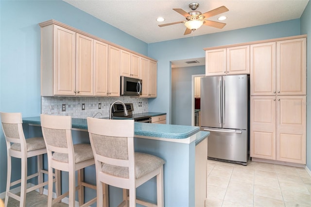 kitchen featuring ceiling fan, decorative backsplash, light brown cabinetry, a peninsula, and stainless steel appliances