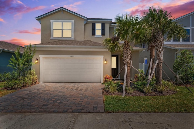 traditional-style home featuring decorative driveway, a garage, and stucco siding