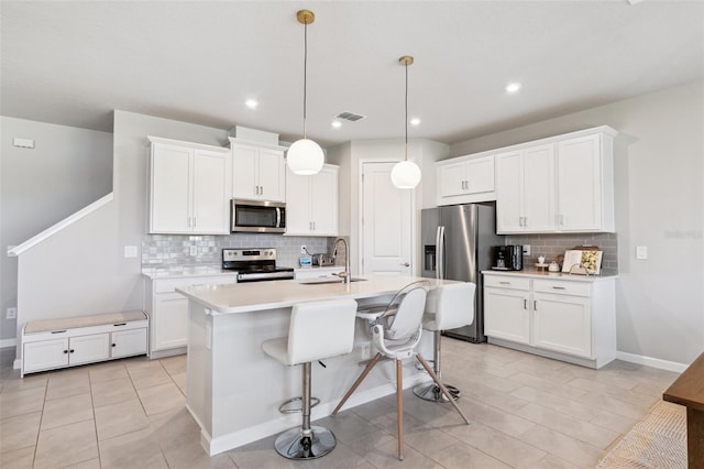 kitchen with backsplash, visible vents, appliances with stainless steel finishes, light countertops, and an island with sink