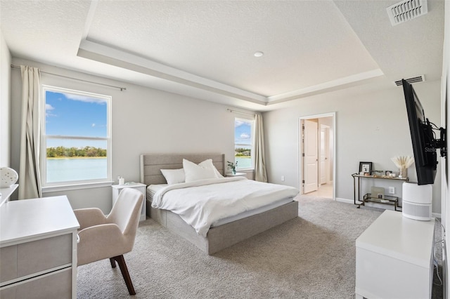 carpeted bedroom with a textured ceiling, a tray ceiling, visible vents, and baseboards