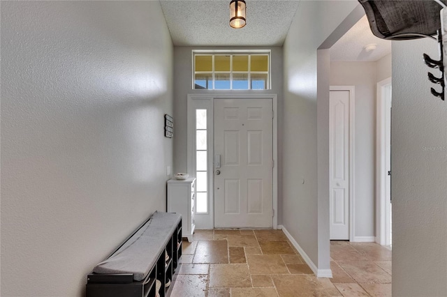 foyer entrance with stone tile flooring, baseboards, healthy amount of natural light, and a textured ceiling