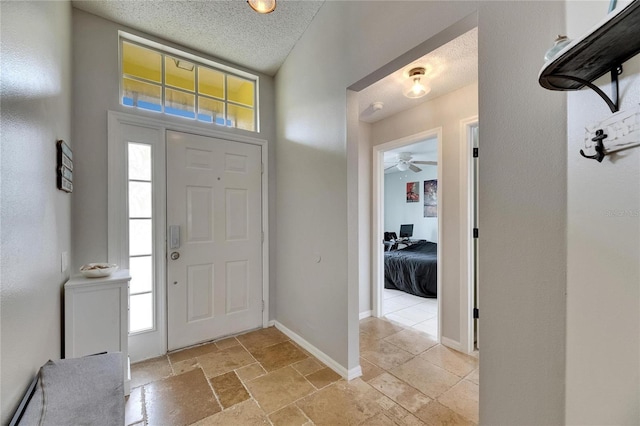 foyer entrance with healthy amount of natural light, a textured ceiling, ceiling fan, and baseboards