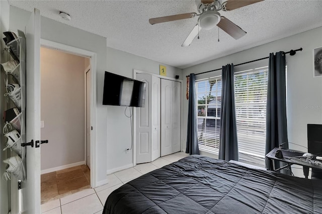 bedroom featuring light tile patterned floors, a textured ceiling, a closet, baseboards, and ceiling fan