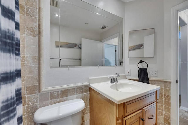 half bathroom featuring tile walls, toilet, vanity, and wainscoting
